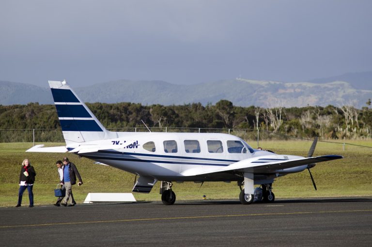 A light aircraft parked at the end of a runway, with people walking away from the plane