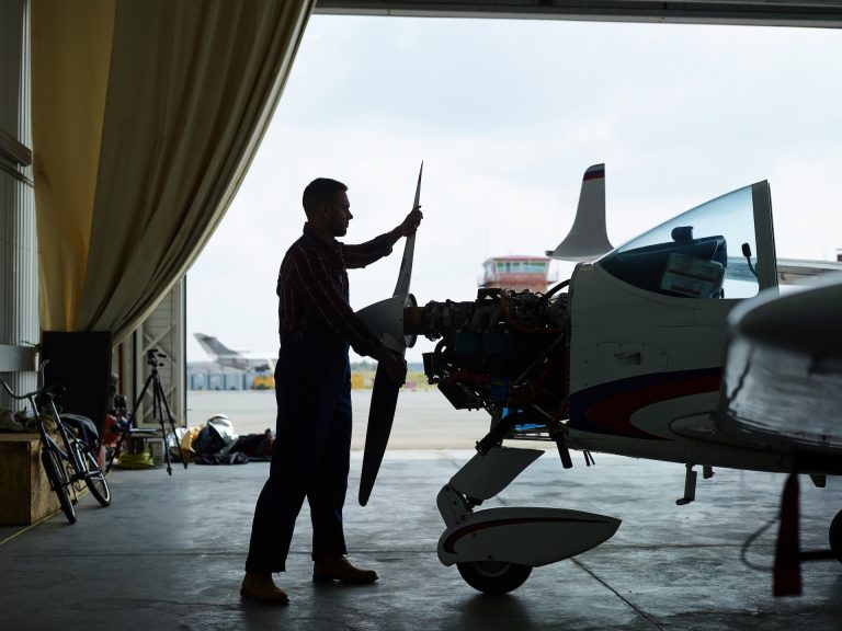 A man standing at the front of a small plane, preparing to turn the propeller to start the engine